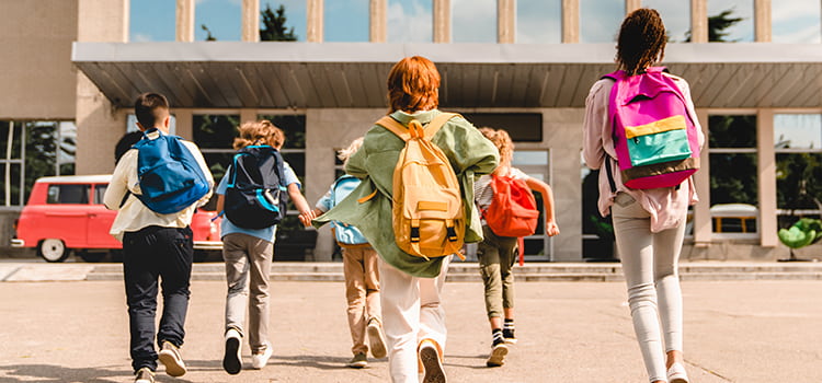 A crowd of students with backpacks run toward the entrance of a building